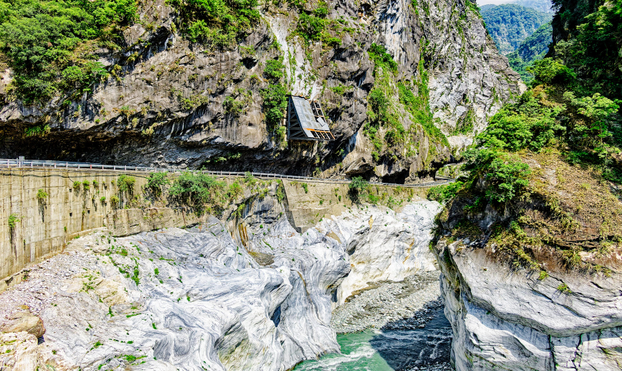 Riverbed with the water dried up to a stream alongside a road in the mountains.