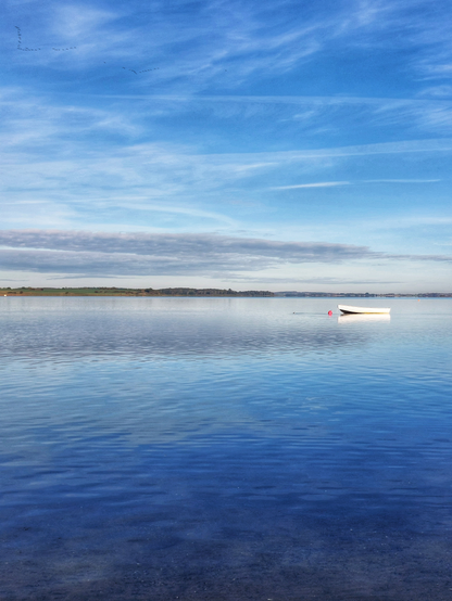 you can see the sea and a white empty boat on it. the sky is blue with a few faint clouds
