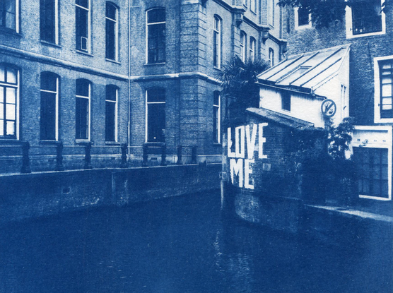 Cyanotype d'un canal amstellodamois et de ses bâtiments en brique qui l'entourent. Sur un muret, l'inscription Love Me.