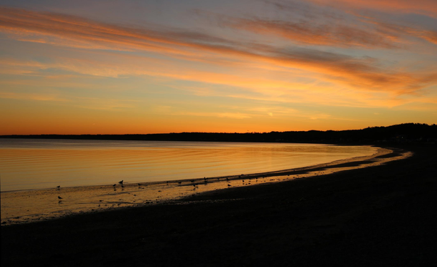 Photograph of an orange sunset over a bay, where the very calm sea reflects the colors of the sky.
Photographie d'un coucher de soleil orange sur une baie, où la mer très calme reflète les couleurs du ciel.
