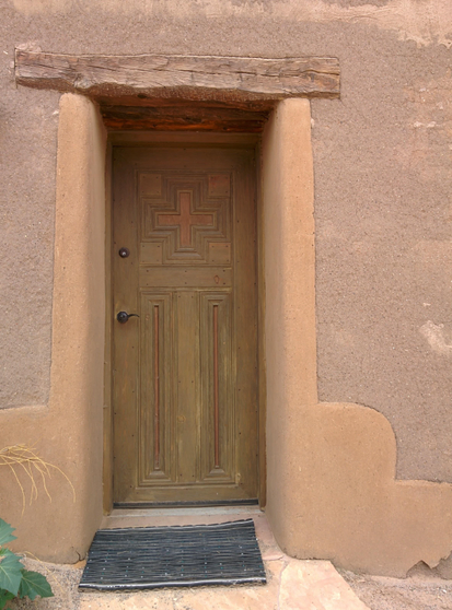 Image: Close up view of a warm beige and brown doorway with adobe plaster and wood details at The Tower Gallery in Pojoaque, New Mexico.