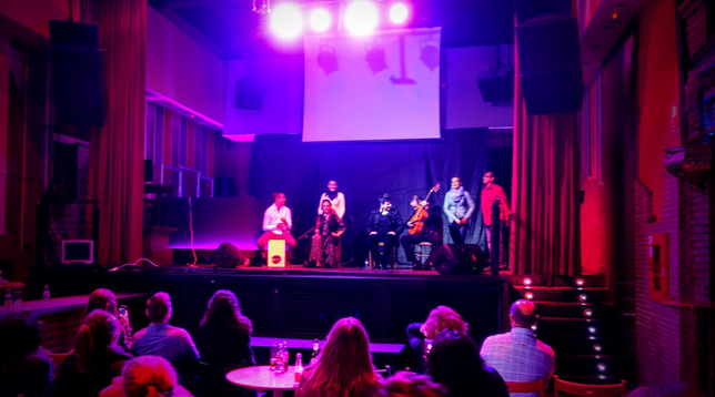 Auf einer Bühne sitzen und stehen verschiedene Musiker und Sänger, die kurz davor sind mit ihrer Flamencomusik zu beginnen... 