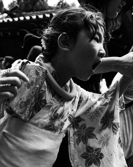 Japanese child wearing traditional suit being dragged by the hand by her mother. The photograph is taken from a close point of view. Her mouth is with open like she is screaming.