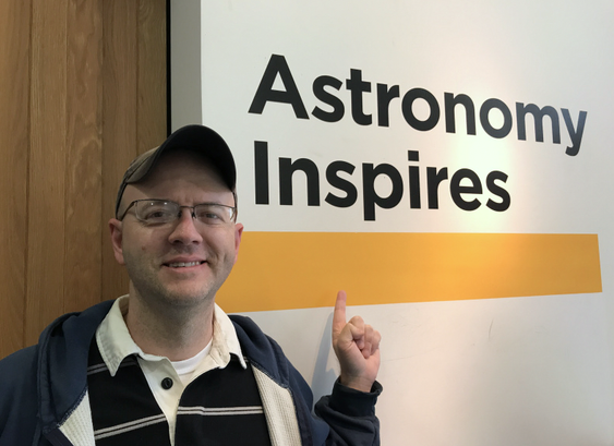 The author stands next to (and points toward) a sign that reads "Astronomy Inspires".