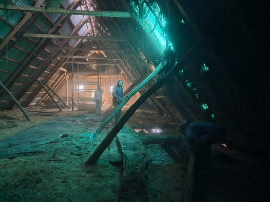 Drei Menschen auf einem Dachboden. Licht fällt durch eine grüne Plane.