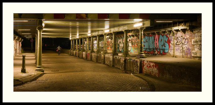 colour - Very early morning shot of a brightly lighted railway viaduct near HS Trainstation. It dates from 1885 and is in neo-Renaissance style. One of the spots in The Hague that is regularly used by graffiti artist. A lone cyclist can be seen exiting the underpass.