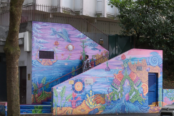 A photo of an outside stairway going right then change to left mid way. The walls of the stairway are heavily painted with multiple colours. A black woman is going down