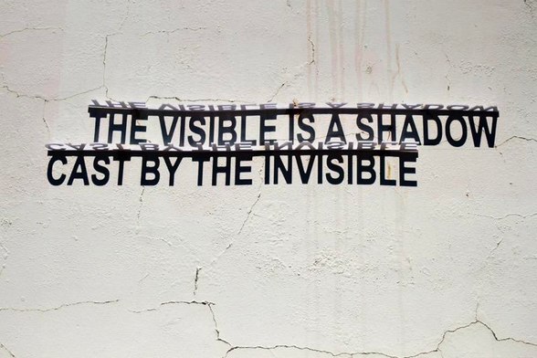 Strijdom van der Merwe's text installation on a white wall that says "the visible is a shadow cast by the invisible"