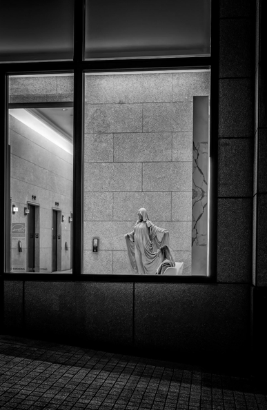 Woman reads while sitting in the lobby of a San Francisco office building at night. Beside her is a statue of a ghostly woman.