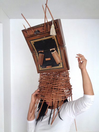 a woman wears a sculptural mask inspired by African ceremonial masks, made from a colonial-era writing desk
