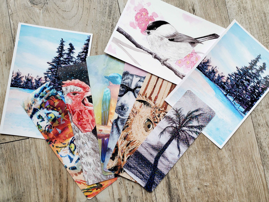 A photo of handmade bookmarks with various artworks (all traditional drawings and mostly animals) and three art prints with white borders.