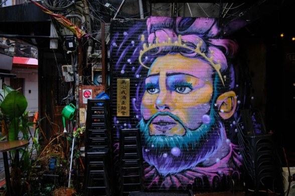 A crazy purple and blue painting of someone's head... on a wall with indistrial grit around.