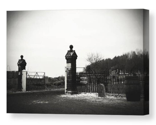 Gloomy black and white photograph of stone gateposts by metal railings.  A sign affixed to the railings warns 'Beware of the Engines'.  The image is shown printed upon a block canvas.