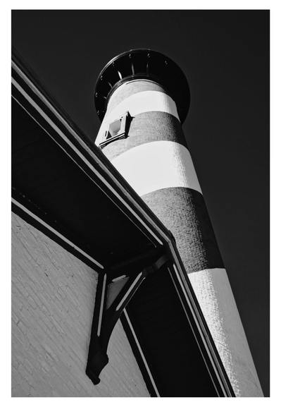 Black-and-white image of a tall lighthouse with bold stripes. Seen from below, the angle emphasizes its height against a clear sky, conveying strength.