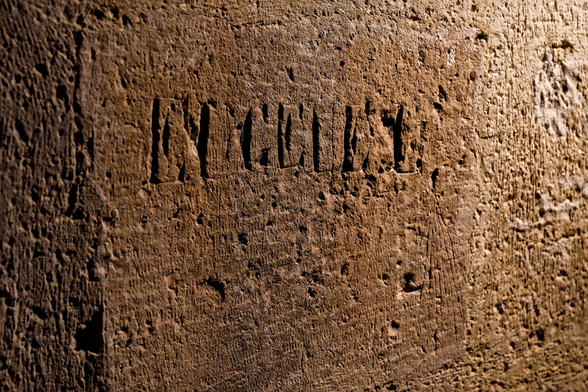 A stonewall lit by an orange light where a name is carved in capital letters, reading “EICEILL” (approx)