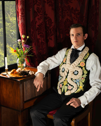 Shae Bishop sits in a stately pose while wearing a vest covered in two snakes and florals, all depicted in tile