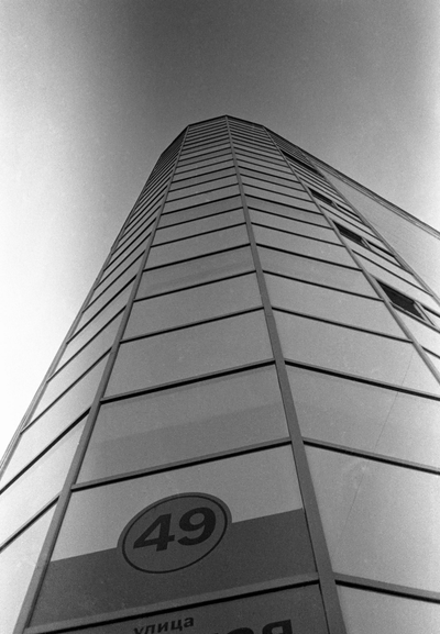 This black-and-white photo shows a modern high-rise building, shot from the bottom up. A sign with the number 49 is visible at the very bottom.