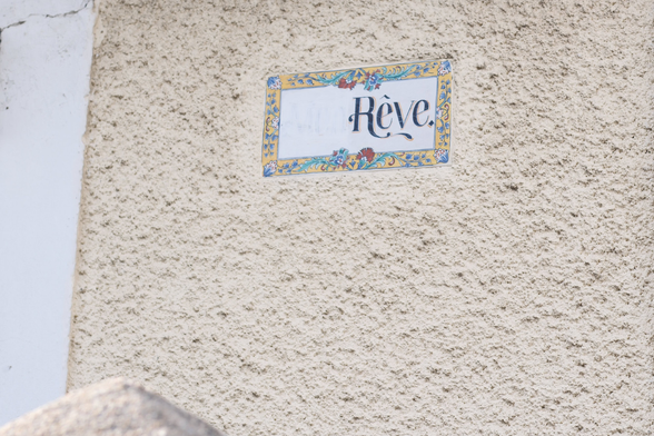 A light coloured wall of a house with a white ceramic sign in it with the word “Rêve” written