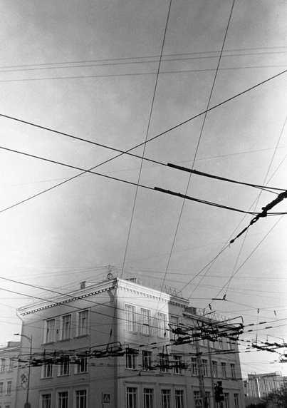 The black-and-white photo shows many intersecting trolley wires against the background of the sky. The upper floors of the building are visible just below.