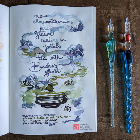 Photo of open notebook next to two glass dip pens. The page shows a haiku written in hazy blue-tinged purple ink with wispy trails as if it were steam rising from a dark black-green tea bowl. The steam also has pale yellow-green flower petal-like shapes blooming from it.
"no chrysanthemums
just steam curling in petals
tea with Basho’s ghost"
- Poetry and art by Maiji/Mary Huang, humangray.com