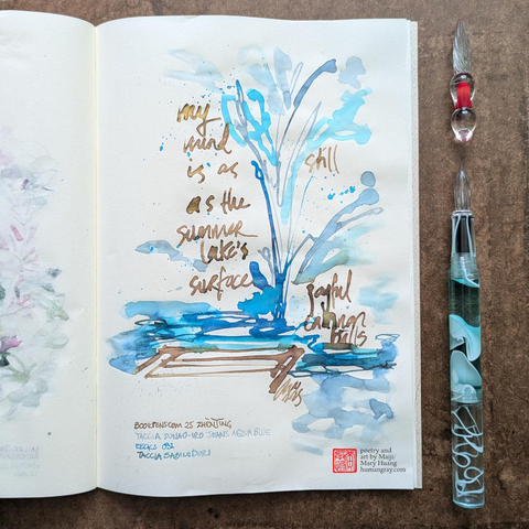 Photo of a haiku illustrated with ink in an open notebook next to two glass dip pens, one of which is just a tip. The illustration depicts a vertical splash of glittering blue water with gold ink words staggered on either side and what appears to be a dock in the bottom left.
"my mind is as still
as the summer lake's surface
joyful cannonball" [the version in the photo says plural "cannonballs"]
- Poetry and art by Maiji/Mary Huang, humangray.com