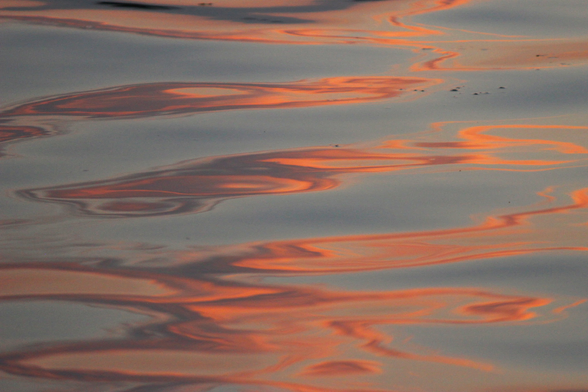 Photograph of peach and grey shapes on a light blue background from light reflected on a lake surface, forming abstract swirls.