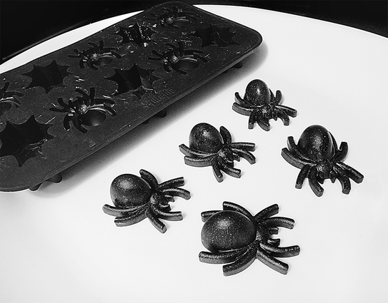 Five dark sparkly resin spiders next to their Killstar silicone mold on a white tray.