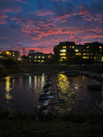 Vista nocturna del río Kame con las luces amarillas de las casas del otro lado reflejadas en el agua negra del río. En el cielo, todavía quedaba un resplandor rosado de la últimas luces del día.