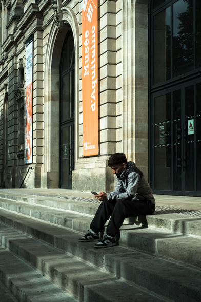 A man waiting on his phone on the steps of a building in the street