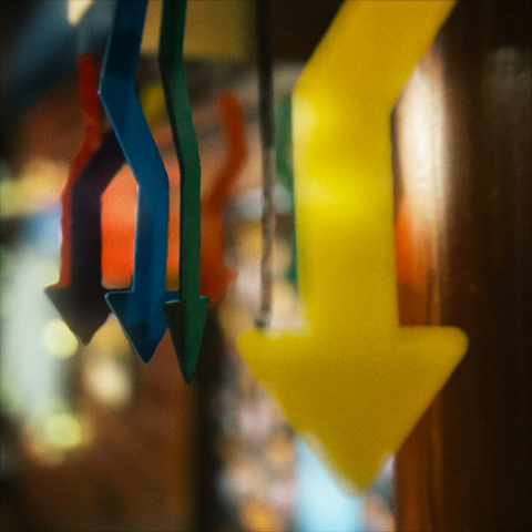 Several plastic hanging arrows of varying colors aim in different directions before ultimately pointing down inside a semi-dark room.