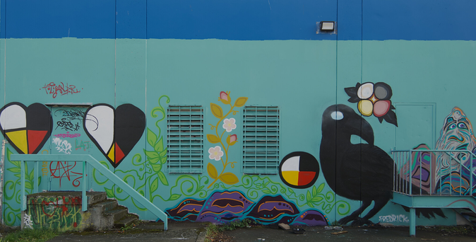 Side of building and its doors all painted blue. The side has a large black bird painted on it plus some four coloured hearts.