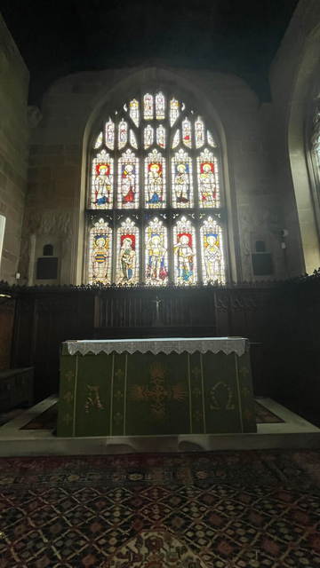 The altar of St Bartholomew's, dressed with a green and gold cloth.  A beautiful stained glass window can be seen above the altar.