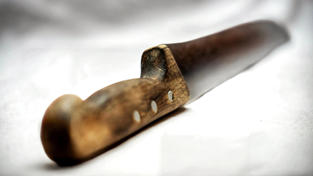 Das Bild zeigt ein altes Messer mit Holzgriff auf weißen Untergrund. Der Griff ist von der Benutzung leicht speckig. Der Focus liegt in der Mitte. Die Klinge verschwimmt im Hintergrund  und der Griff im Vordergrund.