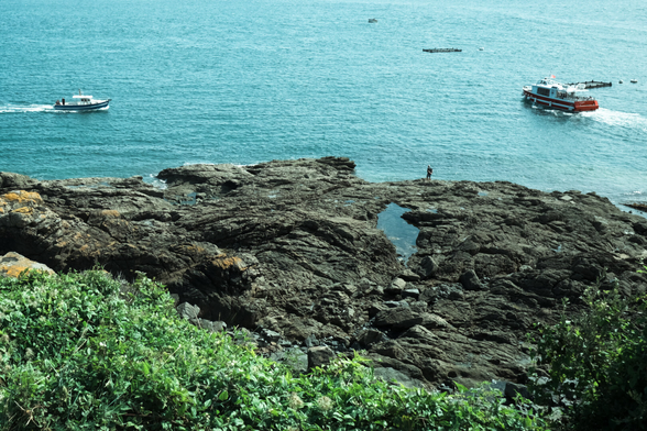 Rocky shore with boats moving and one person standing