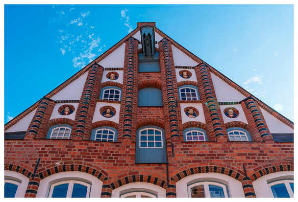 Backsteingebäude mit vielen kleinen Fenstern. An der Außenmauer sind in vertiefungen 6 Büsten untergebracht. Vielleicht zeigen sie die ehemaligen Bewohner des Gebäudes?