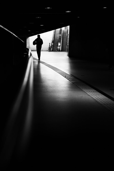 A silhouette of a person in a subway station. Multiple lines lead to the subject.