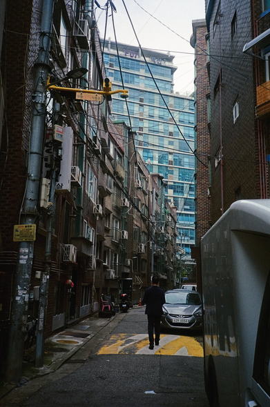 오른쪽으로 완만하게 꺾어지는 주택가 골목 너머로 거대한 마천루가 보인다.