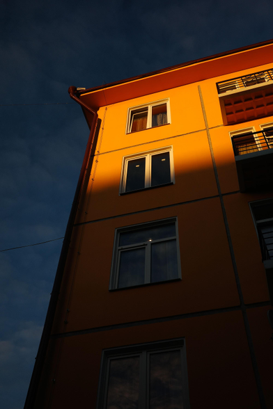 The photo shows a building with bright orange walls and windows illuminated by sunlight. The sky in the background is dark blue and purple, creating a contrast with the warm color of the building.