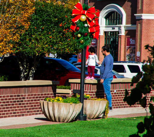 A photo of a father holding a very small child's hand while she stands on a wall in a shopping center mall.