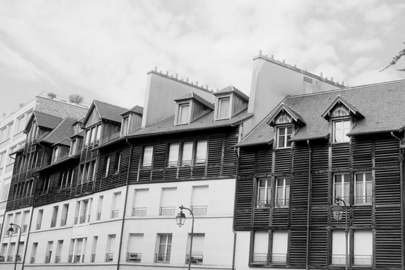 A black and white photo of a parisian building following the street’s curve. Its front has a white part then a black part