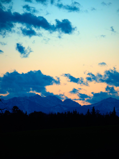 A mountain line with a cloudy sky being lit up by the sunset.