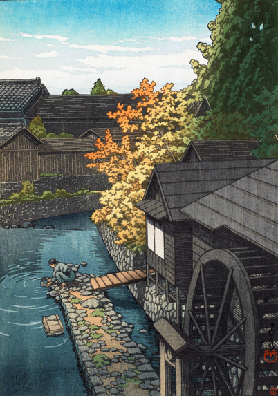 A bright autumn afternoon in Tochigi Prefecture. In the foreground, a watermill stands at the edge of a stone-reinforced embankment bordering a stream. At the end of a narrow stone walkway extending into the water, a female figure crouches low, washing something in a bucket. Just beyond, leaves of tall trees are turning yellow and orange with the season; further on, a group of houses block the horizon. Above, a few white clouds cross a blue sky.