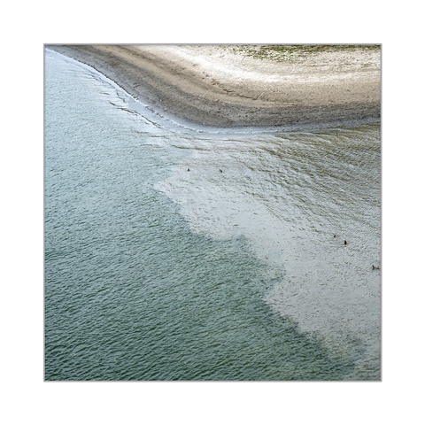 A bay flowing into a river, photographed from above from a bridge. The meeting of two different colored waters creates a beautiful pattern.