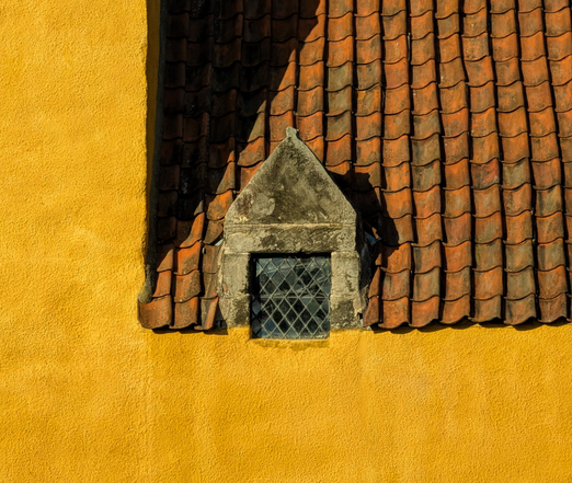 Image shows a vivid sunflower yellow coloured building, clearly quite old with  Tuscan style roof tiles and an old leaded window