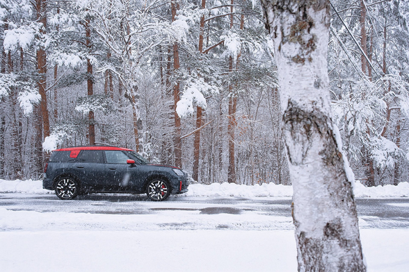 MINI John Cooper Works car, in black and red, on a snowy road in Karuizawa, Nagano, Japan. Against a backdrop of snowy birch trees. Shot past a tree in the foreground.