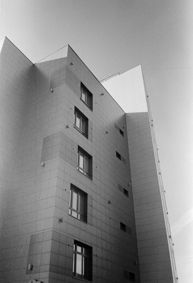 The photo shows a building with a modern architectural design. The building's facade is made of a light-colored material, most likely concrete or stone, and features geometric shapes with protruding elements. The windows are arranged in a staggered pattern, giving the building a dynamic appearance.