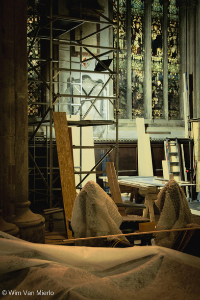 The church during restoration work. Various objects are covered in dust sheets.  A scaffolding has been erected next to the stained glass window; beneath the window is a tressle table.