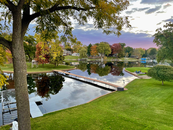 Sunrise photo of a small lake in the fall. There are dark clouds with a pink underside and fall colors in the trees.