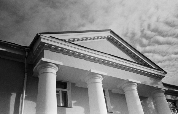 In the black-and-white photo, the upper part of the building is designed in a classical style, with columns and a triangular pediment.