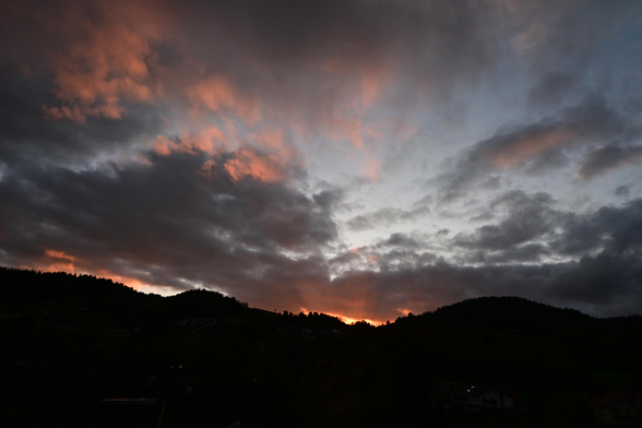 Sonnenuntergang mit aufgebauschten dunklen Wolken und einem orangefarbenen Leuchten über Bergen.